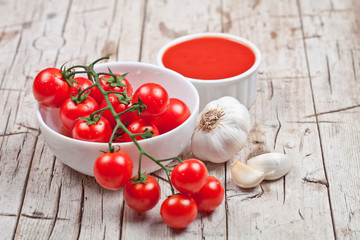 Fresh tomatoes in white bowl, sauce and raw garlic on rustic wooden table.
