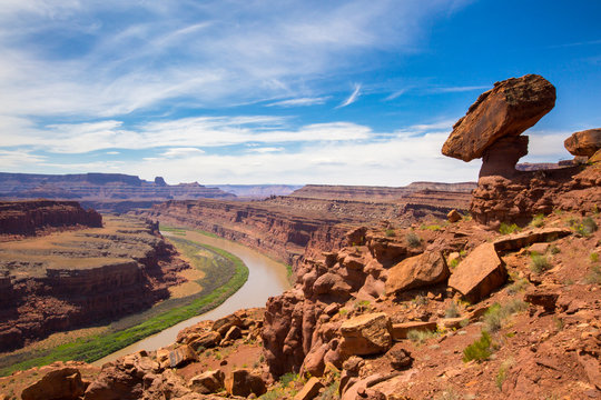 A balanced rock sits over a bend in the Colorado River from a viewpoint at the end of the short 0.3 mile Gooseneck Trail in Canyonlands National Park, Utah. The La Sal Mountains are in the distance.