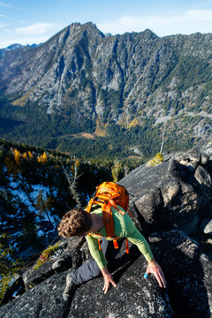 A man with a pack traverses an exposed rocky ridge amidst fall colors near Colchuck Lake in the Cascade Range of Washington State.
