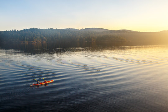 Two tandem kayakers paddle into the early morning light near Harney Channel while on a 3-day sea kayaking trip in the San Juan Islands. The photo was taken from Blind Island, a small 3 acre state park near Shaw Island that offers camping opportunities to human and wind-powered boats.