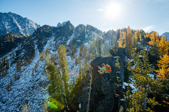 A man with a pack traverses an exposed rocky ridge amidst fall colors near Colchuck Lake in the Cascade Range of Washington State.