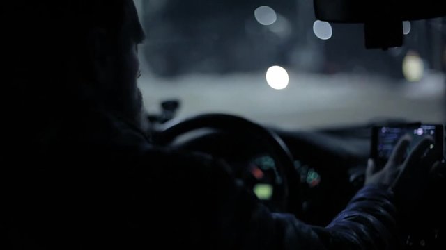 A man gets into the car and turns on the navigator on the smartphone