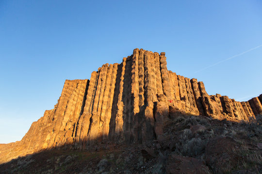 A man stands under the Sunshine Wall of the Frenchman-Coulee at sunrise in central Washington State. The impressive volcanic basalt columns are the remnants of lava flows that cooled once reaching the surface. The unique features of the columns make them a popular choice for rock climbers.