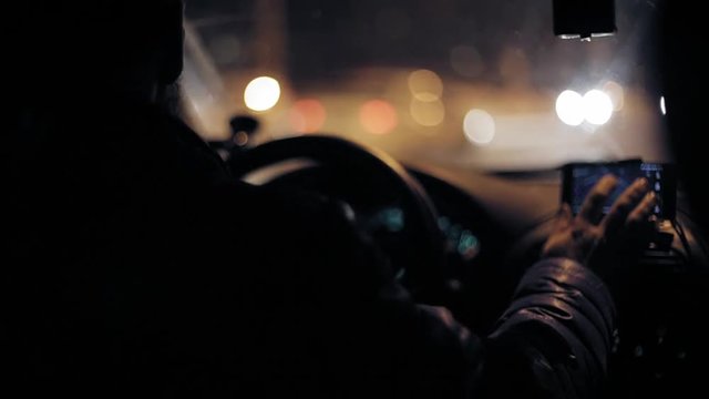 A man gets into the car and turns on the navigator on the smartphone