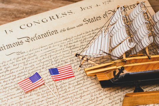 American flag and ship made of wood and fabric handmade on the background of an excerpt from a copy of the document of 1776 on the signing of American independence
