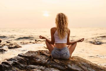 Fototapeta na wymiar Young woman practicing yoga at the beach sea view at sunrise or sunset outdoors. Harmony and meditation concept. Healthy lifestyle