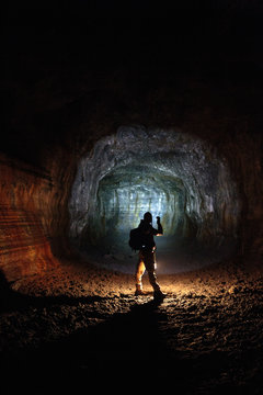 A male caver holding a propane lantern and flashlight while exploring the 13,042 foot long Ape Cave near Mount St. Helens in the Gifford Pinchot National Forest of western Washington State. The cave is the third longest known lava tube in North America. The cave is open year round and has a easier, shorter lower cave section and a slightly more physical and longer upper cave section.