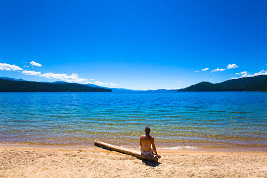 A woman takes in the view while sitting on a drift log at a swimming area near Reeder Bay Campground on the west end of the pristine and beautiful Priest Lake in north Idaho.