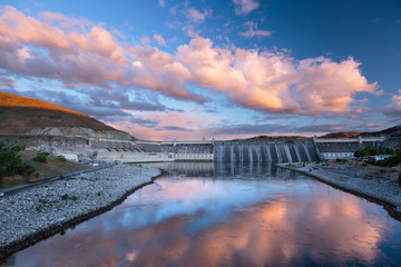 Grand Coulee Dam in central Washington State under a colorful sunset. The dam is the largest capacity power station in the U.S.  The nearby Franklin Delano Roosevelt Reservoir provides water for the irrigation of 670,000 acres of farmland in the Columbia Basin. 3,000 people were forced to relocate before construction and numerous First Nation ancestral land sites were flooded. The monumental project was one of a variety of FDR era New Deal projects.