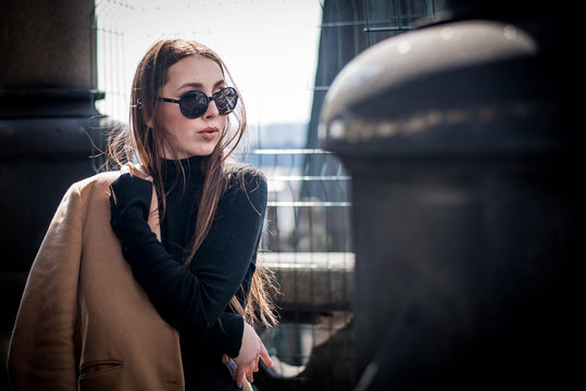 Young Beautiful Woman With Long Brown Hair In Sunglasses On A Walk On A Cloudy Day. Fashionable Sexy Girl. Street Fashion Look. Cute Student