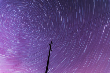 Stars spinning in circle creating light trails with silhouettes in foreground. Night sky in vivid...