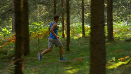 Young Caucasian sportsman exercising by trail running through the cool woods