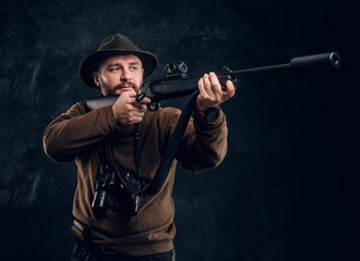 Fototapeta premium Hunter holding a rifle and aiming at his target or prey. Studio photo against dark wall background