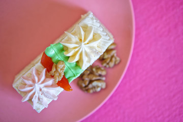 Rectangular pastry with protein cream and walnuts in a plate on a pink background