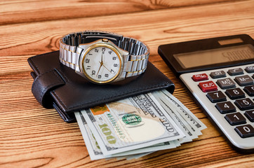 wrist watch with dollars and calculator on wooden background