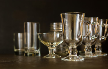 Several glasses and glass cups on a dark background. Blurred background.