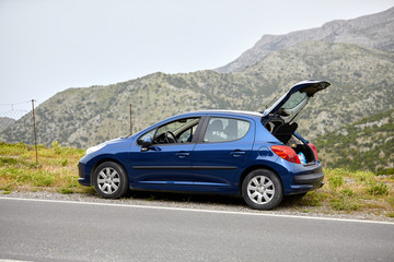 a new blue car with an open trunk stands on the side of a mountain road
