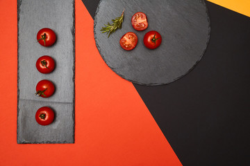 Ripe cherry tomatoes and rosemary composed on black slate boards on colorful background