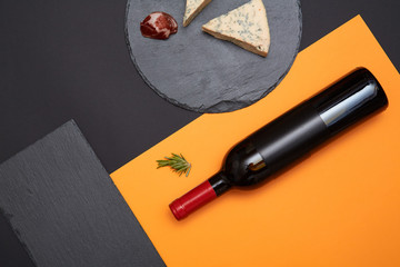 Layout of blue cheese with prosciutto slices on black slate board with bottle of wine on colorful...