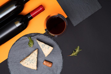 Composition of blue cheese with prosciutto slices on black slate board with bottle of wine on...
