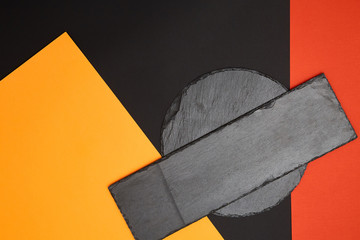 Composition of empty black slate serving board on multicolored background with geometric composition