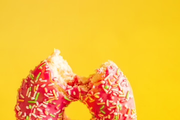The taken a bite pink donut on yellow background, closeup