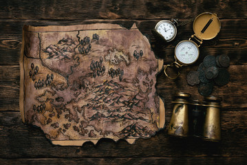 Old map, compass, binoculars and a pocket watch on a adventurer table background. Treasure hunt concept.