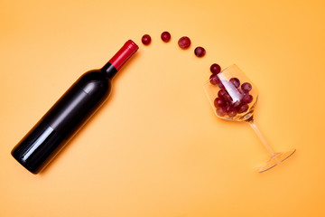 Composition of grapes flying from bottle of wine into shiny wineglass on yellow background