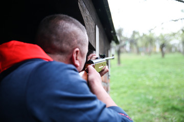 a man with a rifle stands for a corner building in ambush waiting for his target