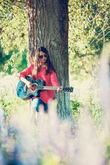 Beautiful woman near the tree and the field with lupine playing guitar