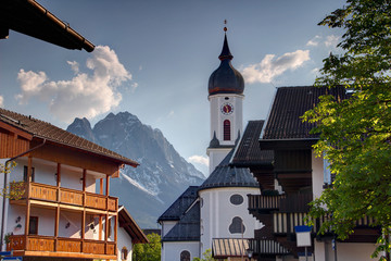 Church St Martin with onion dome in old historic center of resort town Garmisch Partenkirchen and sharp rocky Zugspitze peak in sunny springtime, Wetterstein range Bavarian Alps Bayern Germany Europe