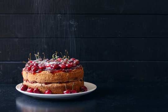 Homemade cake topped with whole cherries and powdered sugar