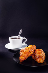 cup of black coffee and croissant on black