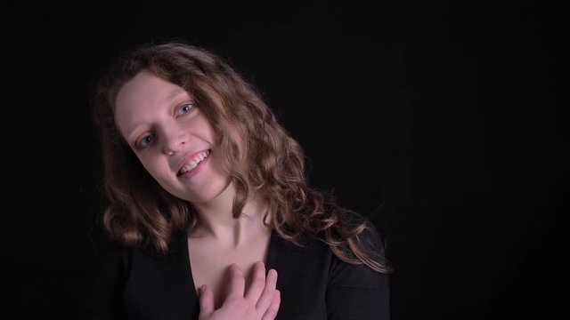 Portrait of young curly-haired girl shows suprise and gladness into camera on black background.