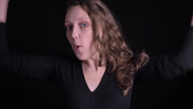 Portrait of young curly-haired girl shows extreme happiness and raises hands in gladness into camera on black background.