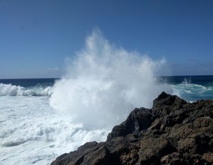 Fototapeta na wymiar Welle bricht sich an einem Felsen im Wasser