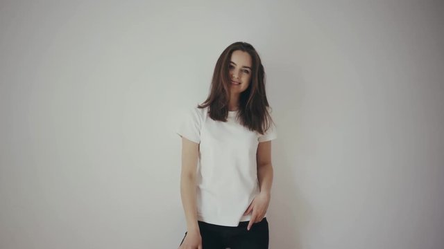 Beautiful young slim brunette girl posing in front of the camera in white blank t-shirt and black jeans, white isolated background, showing the back and front for the mock-up, smiling happily