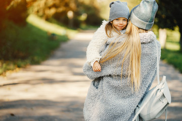 young blonde mother holding her toddler daughter in her arms as they are walking through the park on a sunny day