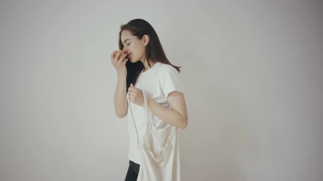Young hipster smiling girl with white blank cotton shopper tote bag wearing white t-shirt and black jeans, mock-up of blank bag, white wall on the background, concept of shopping
