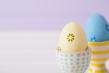 Closeup two colorful painted Easter eggs in vibrant modern egg stands on pastel lilac background.