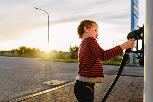 Child holding the hose of a fuel pump at sunset at a gas station.