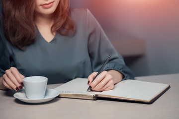 young adult female has coffee break in cafe and writing notes in diary or notepad;