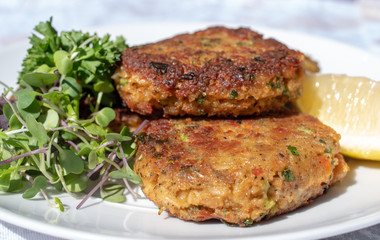 Crab cakes on the white plate with lemon and microgreens.