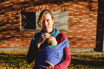 mother lovingly carrying her newborn baby in a sling scarf during a sunset stroll in front of red...