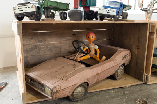 Old vintage toy car with doll in a wooden box. Other toy cars on top.