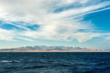 Seascape, view of the blue sea with high bald mountains in the background