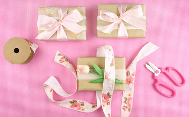 Gifts wrapped in kraft paper and pink ribbons overhead flat lay for Mother's Day, birthday or Valentine's Day celebrations.