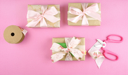 Gifts wrapped in kraft paper and pink ribbons overhead flat lay for Mother's Day, birthday or Valentine's Day celebrations, with copy space.