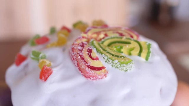 a traditional Easter cake glazed and decorated with marmalade and candied fruits is rotating in beautiful glass plate on wooden background in slow motion close-up 4K video with no people
