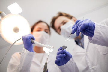 Blurred image of two dentists holding instruments while treating patient, copy space